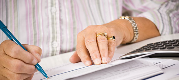 An older woman writing a check to make either a one time or recurring tax-deductible donation to help spread God's word.