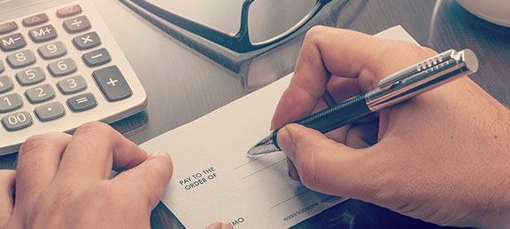 An older woman writing a check to make either a one time or recurring tax-deductible donation to help spread God's word.